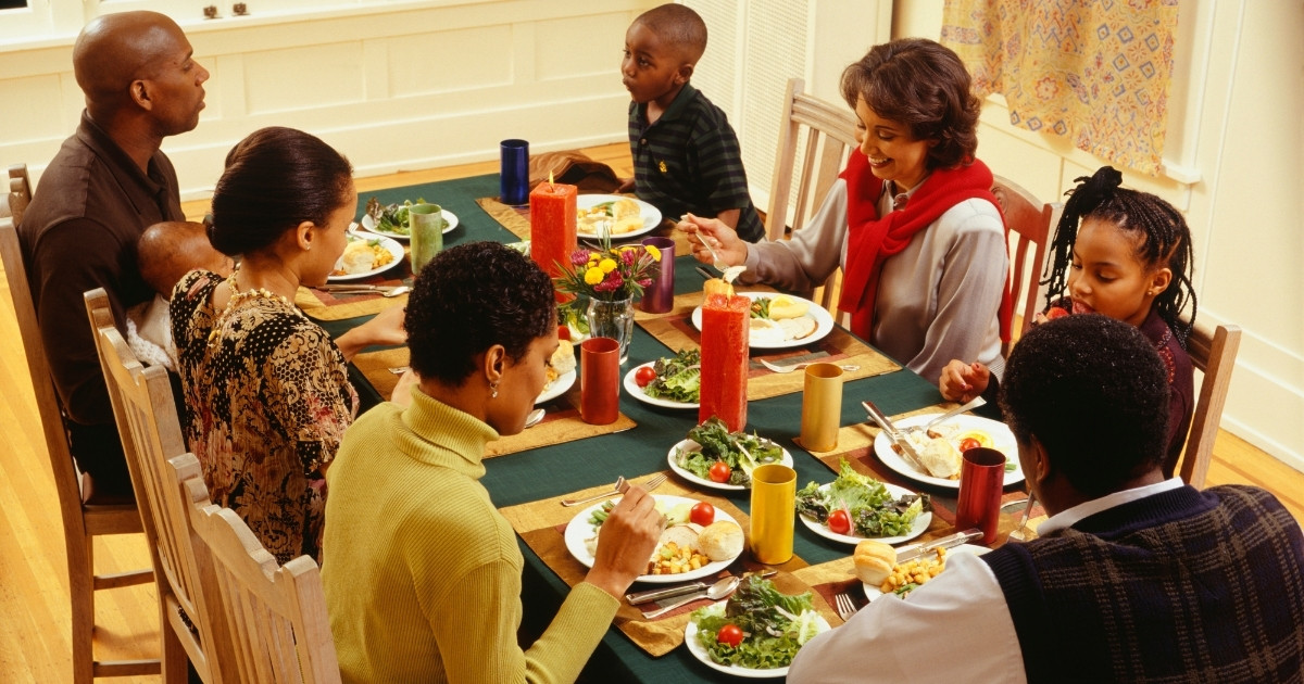 A family sits around the dining room table to eat Thanksgiving dinner.