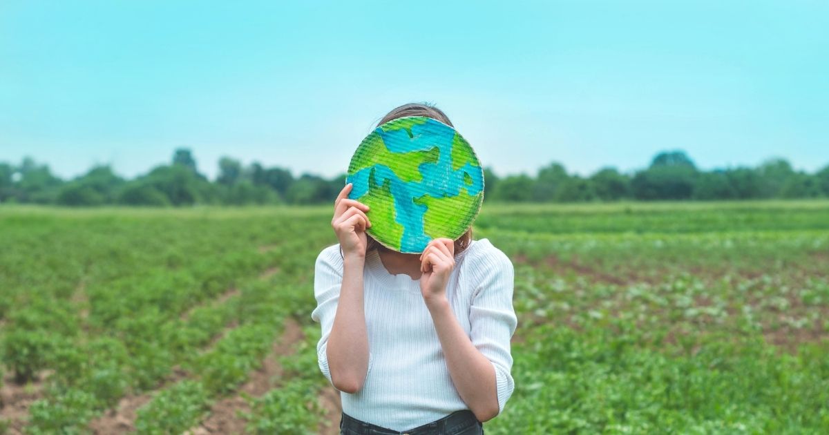 earth_day_website_properties_img_extension_1200x630 A child holding up a cutout of Earth, standing in a field.