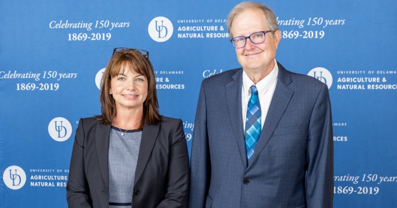 Anna Armstrong and Calvin Keeler pose in front of a University of Delaware step-and-repeat banner.