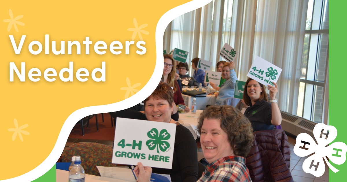 A photo fo a group of adult volunteers sitting in a large room smiling and holding 4-H signs