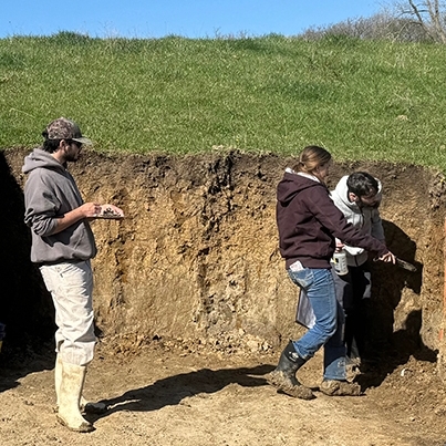 UD students sitting and standing around at a soil site.