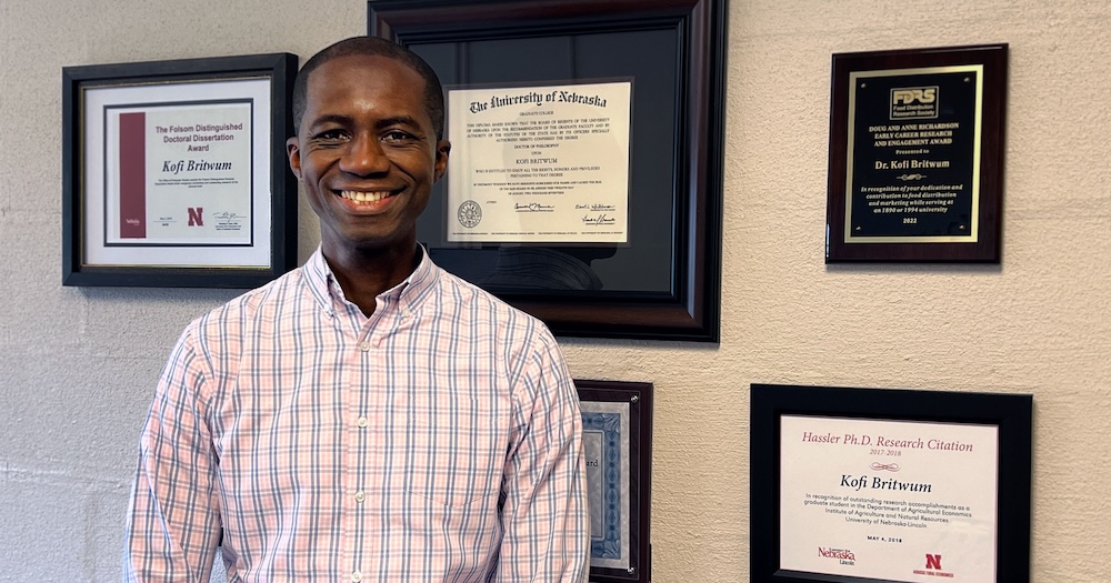 Kofi Britwum stands in front of his awards and plaques.