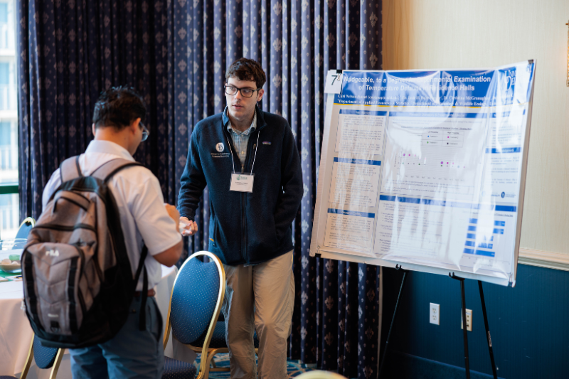 Untitled design - 3 Carl speaks to a visitor at a poster presentation.