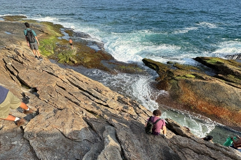 A student sitting on rocks surrounded by water, sketching in a notebook.