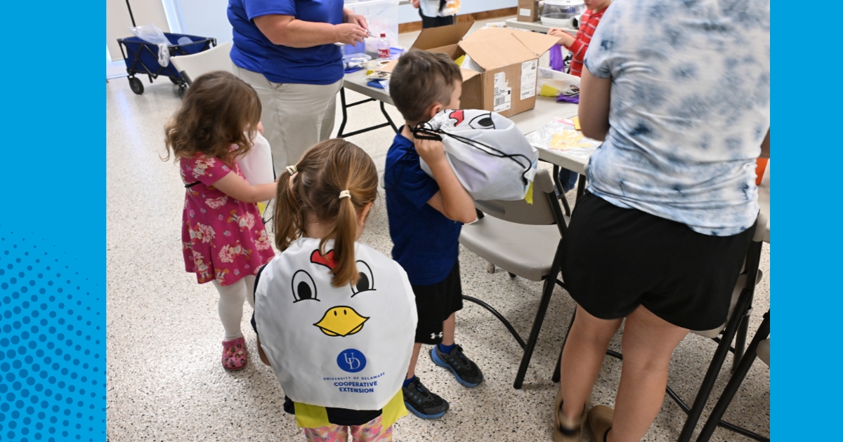 Children standing around a table wearing poultry backpacks