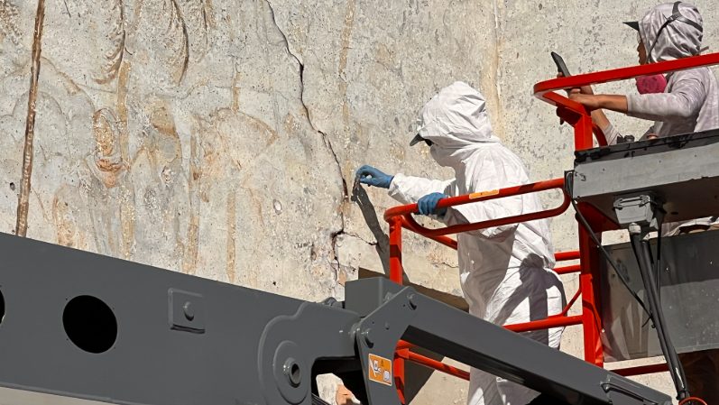 A person in all white protective gear takes a sample of the mural for further testing and analysis. 