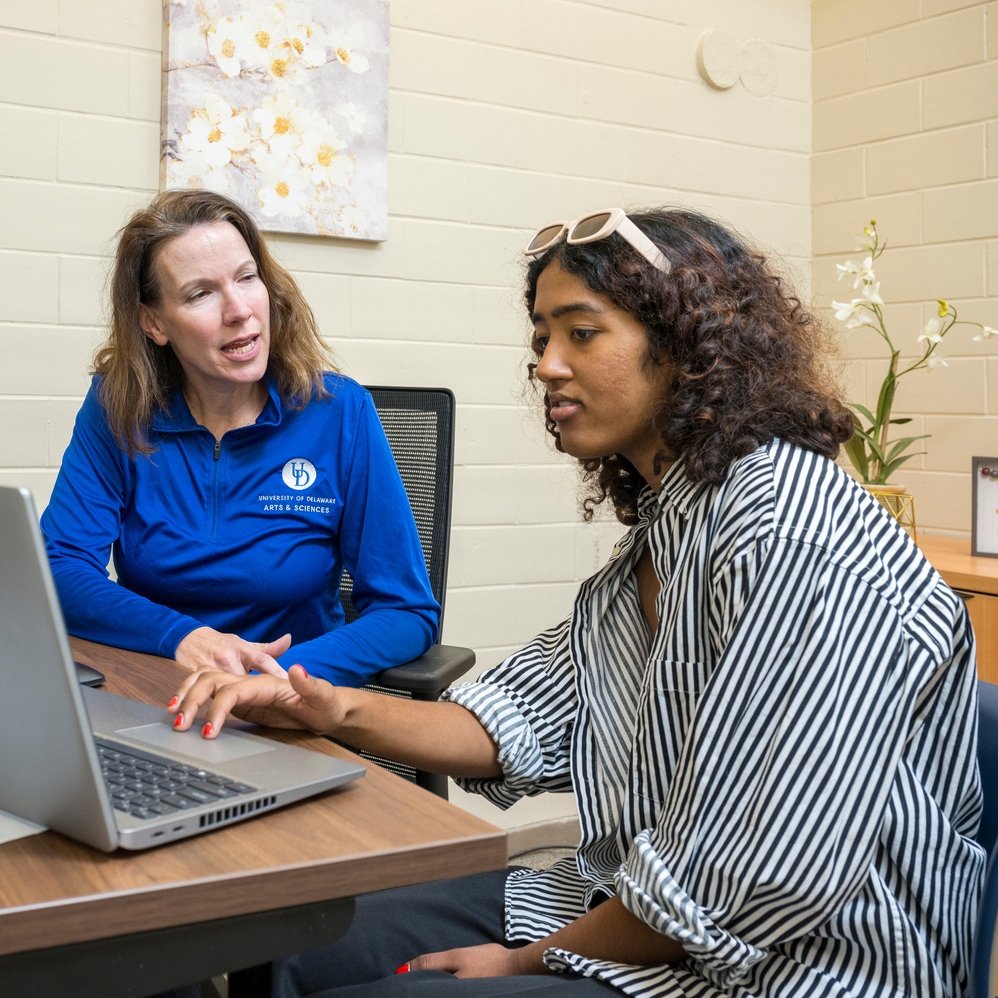 A female University of Delaware student works on her laptop while talking to an advisor inside an office at the Student Success Center.