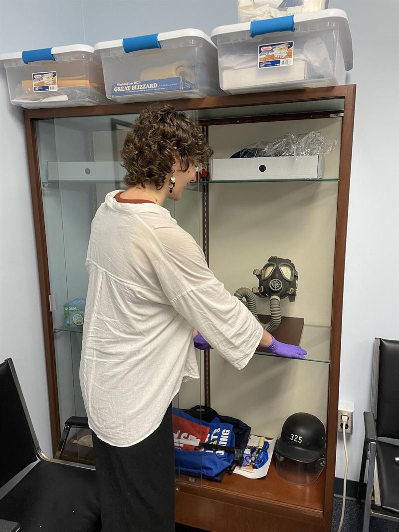Gianna placing the newly mounted mask back in the display case Student putting mask on shelf