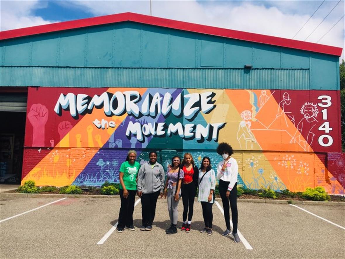 community members and interns visiting a non-profit preserving plywood protest murals community members standing in front of mural