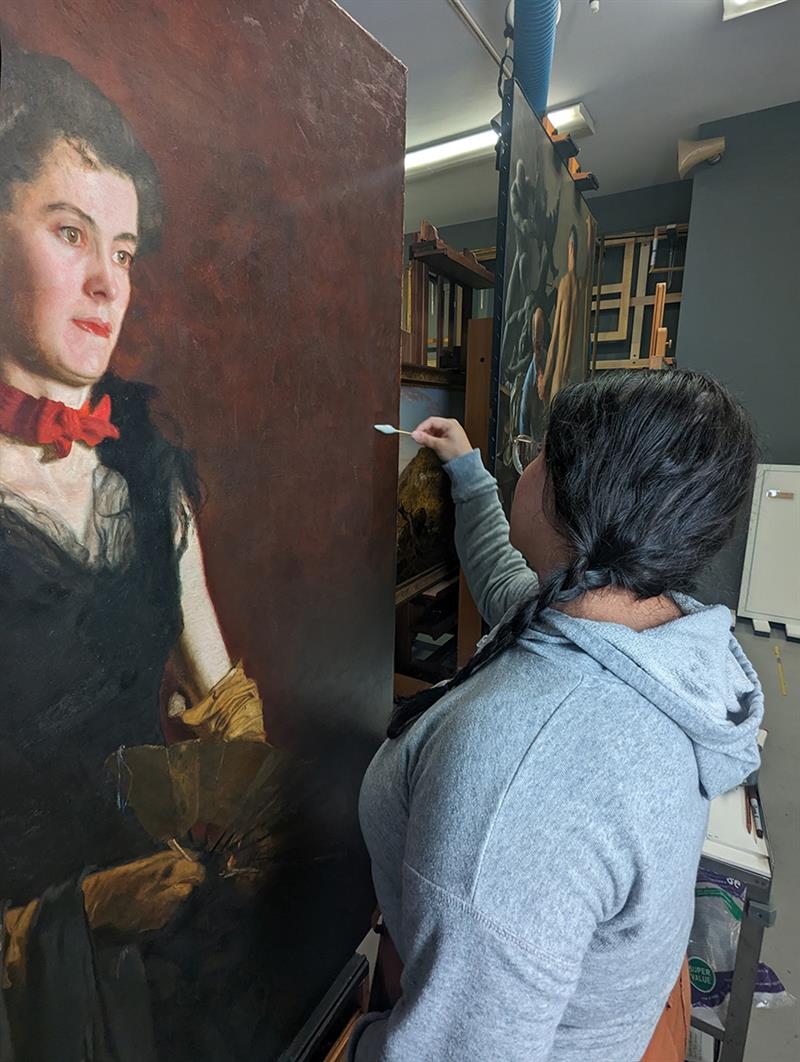Adriana Benavides aqueous cleaning surface of Letitia Wilson Jordan with a swab. Students cleaning surface of painting with a swab