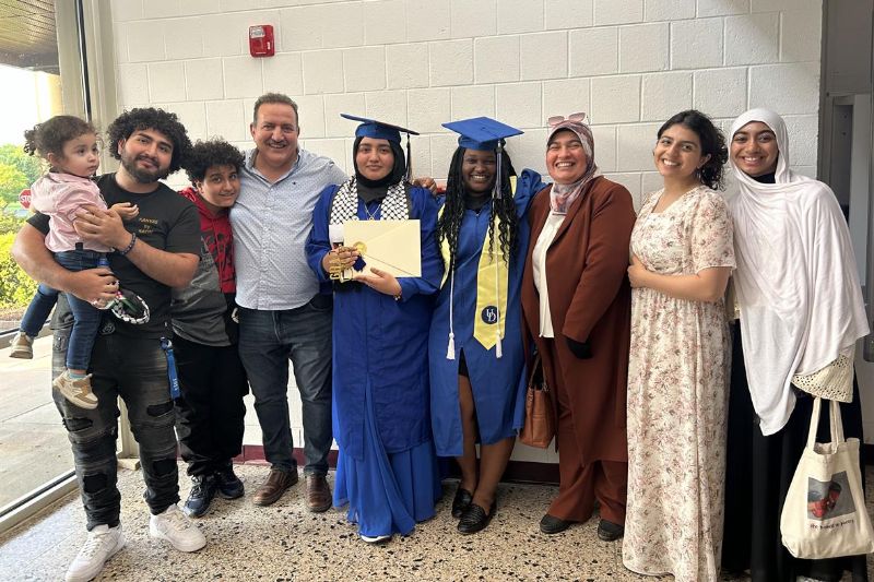 UD AAP graduates and their families, two students are standing in cap and gown with certificate