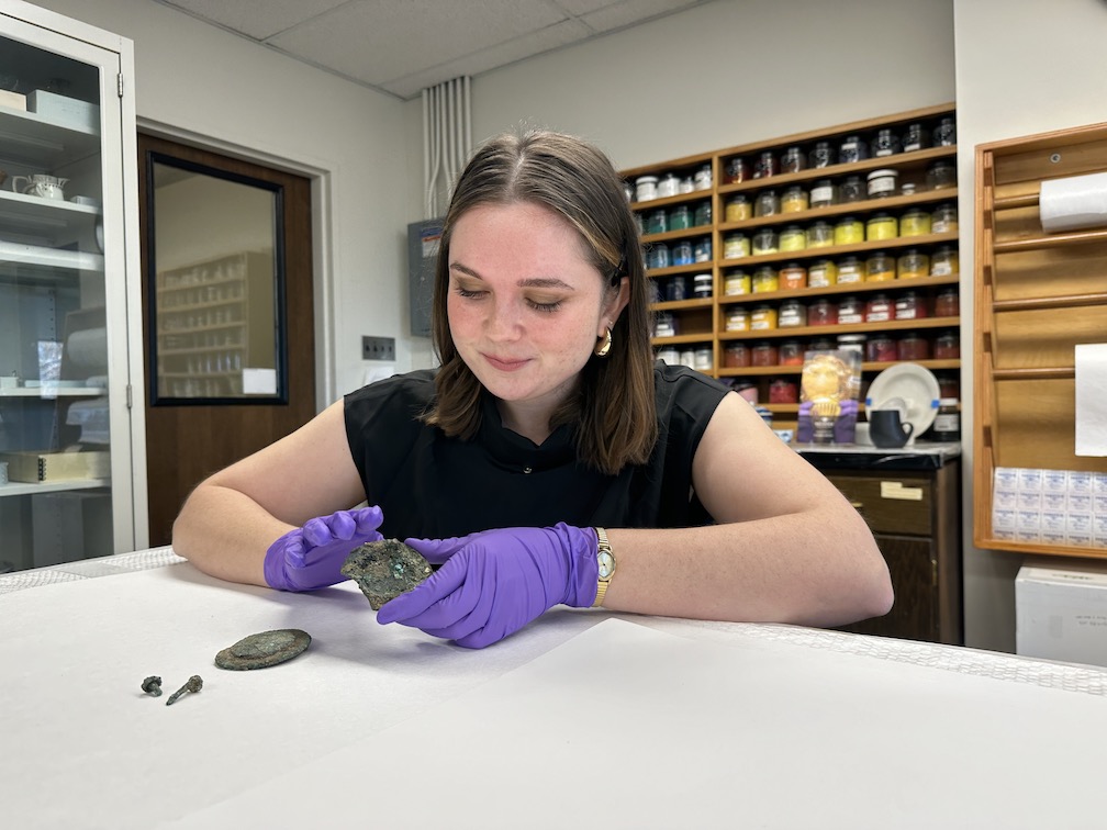 The student holds a small metal object and looks at it. Another small metal object sits nearby on the table. The student holds a small metal object and looks at it. Another small metal object sits nearby on the table.
