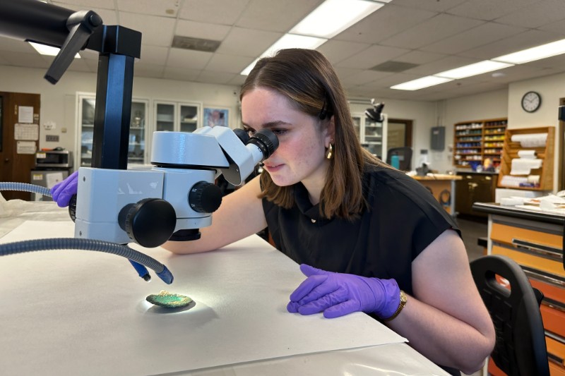 White female students wearing latex gloves looking into a microscope in an art conservation studio