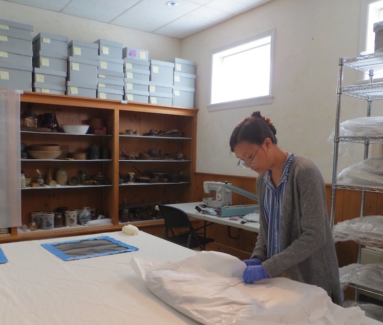 WUDPAC Class of 2026 Fellow Binh-An Nguyen unbagging a garment that has been frozen and preparing it for vacuuming and rehousing. WUDPAC Class of 2026 Fellow Binh-An Nguyen unbagging a garment