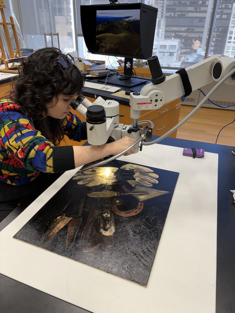 Emily examines a painting by Marsden Hartley under microscopic magnification. student examining art through microscope