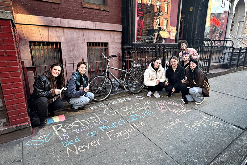 Students posing next to chalk on sidewalk