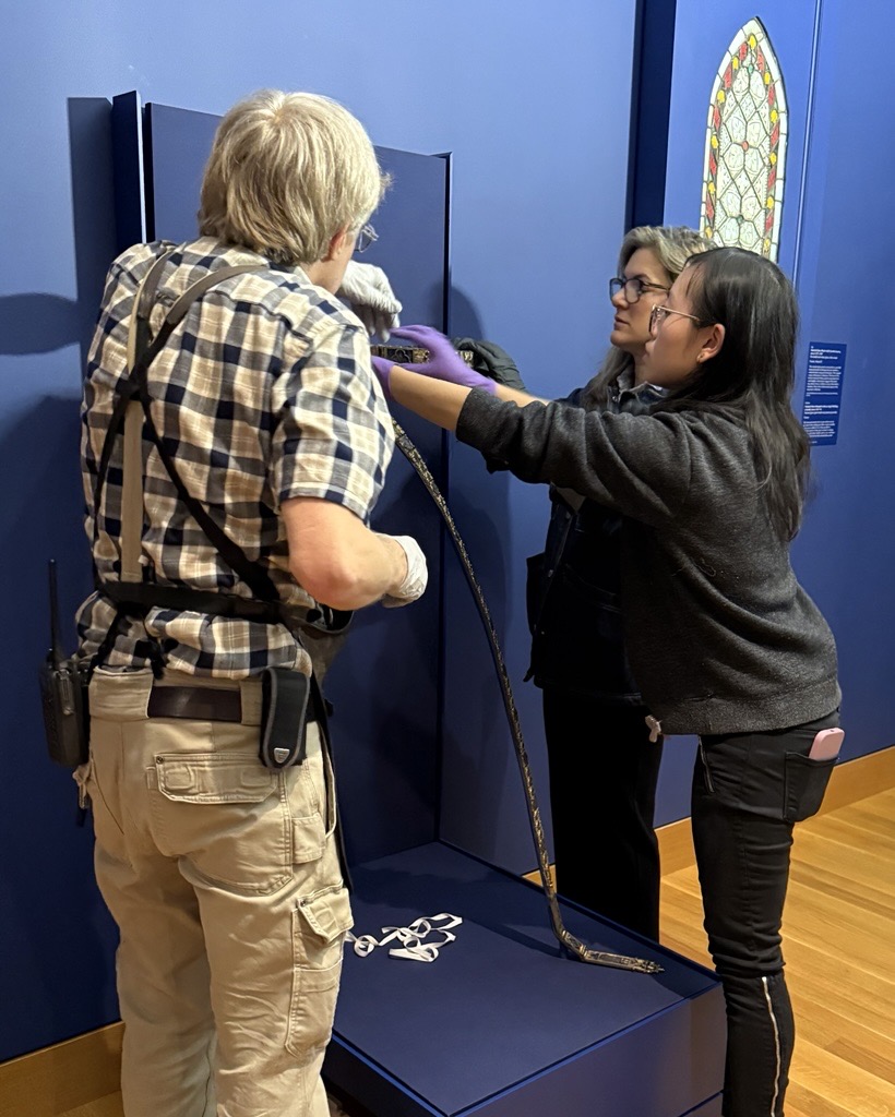 Mount maker Philip Brutz Head of Objects Conservation Beth Edelstein, and Christy Ching installing the belt in the Late Medieval galleries. Three people installing artwork
