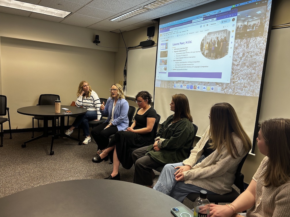From left, Kat Locke-Jones, Laura Peer, Lisa Alexander, Tara Jensen, Caitlyn Kirk and Emily Fishel. Six women sitting in chairs talking inside a conference room during a presentation.