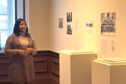 A college student stands next to a museum display and delivers a presentation.