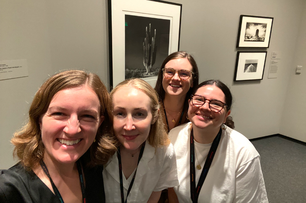 Four smiling museum curators gather for a group photo inside a museum gallery.