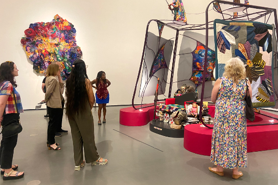 A group of museum patrons examine a large, colorful contemporary sculpture.