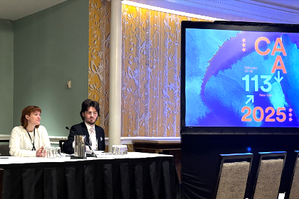 Two college students sitting at a table with a large projector screen next to them.