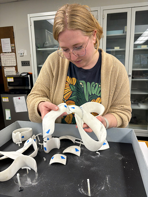 Student in laboratory examines fragments of fractured marble ribbon sculpture.