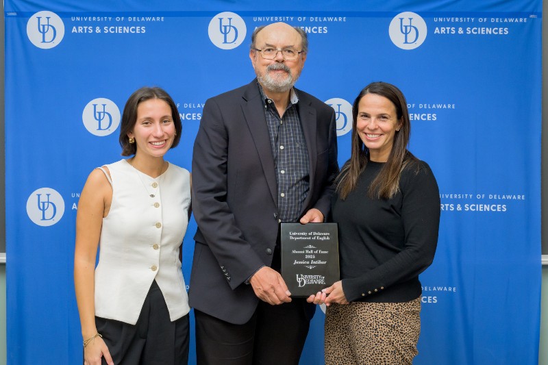 Three smiling people standing in front of a blue background with the University of Delaware logo with the man  and woman on right holding an award plaque.