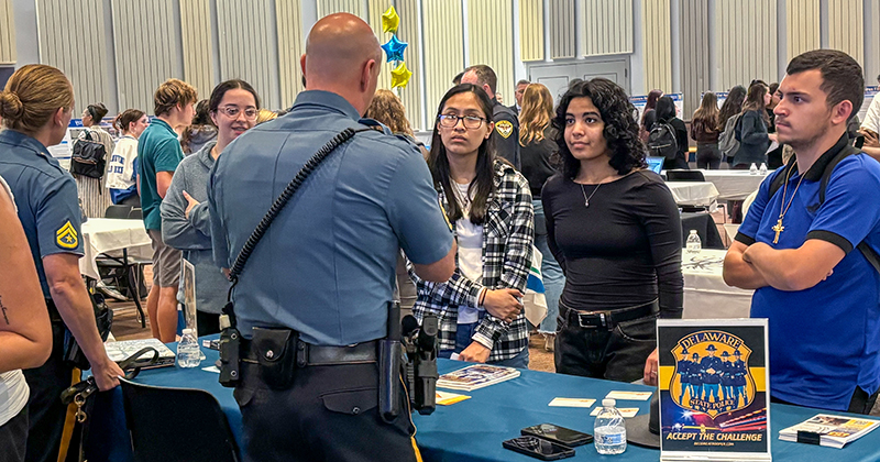 Table presenters University of Delaware internship symposium Student Success Center College students inside a crowded student center listen to a presentation by a Delaware State Police officer during an internship symposium.