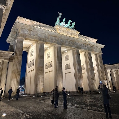 Tourists visit a large marble monument with tall columns at night.