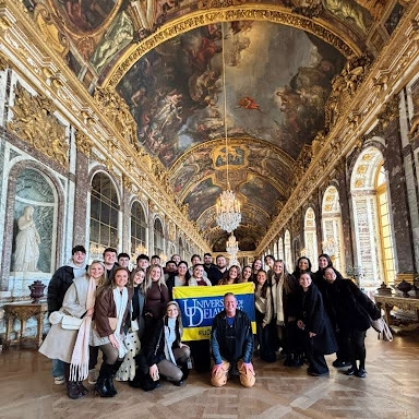 A group of college students and the study abroad program director inside a historic museum with a ceiling mural and sculptures. 