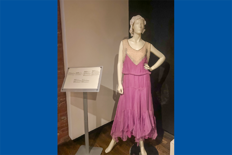 A mannequin in a museum gallery dressed in a dark pink 1920s dress.