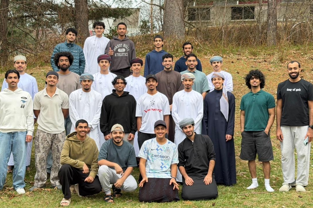 About 20 Omani men stand in a group and smile for the camera outside.