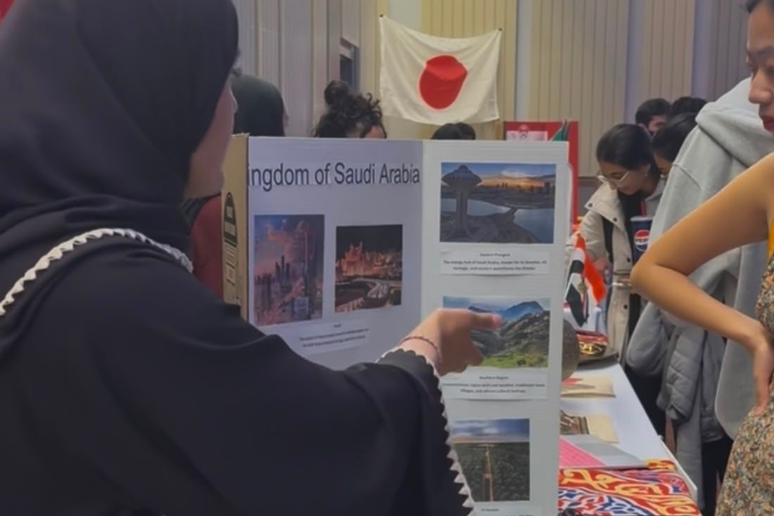 Lena points to a poster board about Saudia Arabia to show information to a student while at her booth at the Festival of Nations.