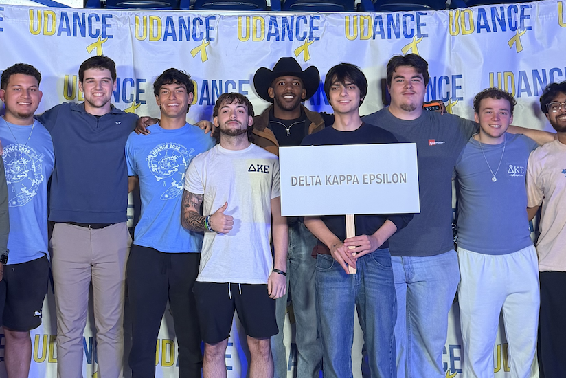 A group of boys in the Delta Kappa Epsilon frat gather to celebrate at the UDance event. One holds up a sign with the name of the frat on it. 