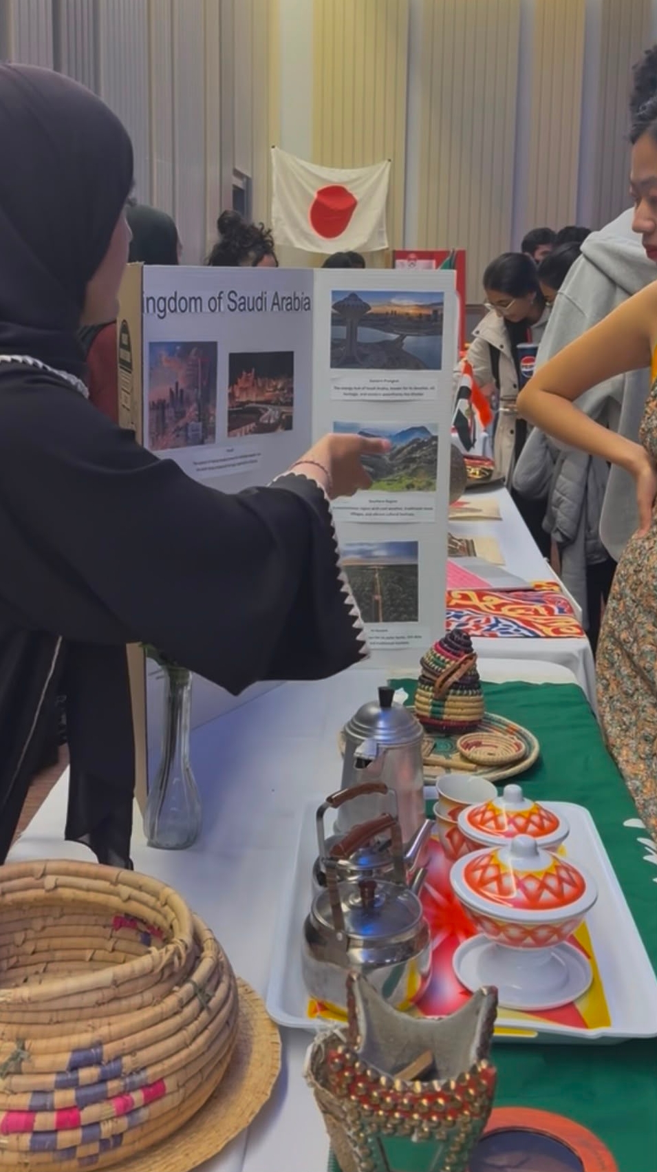 Alrowais points to a trifold poster presentation on Saudi culture, which sits on a table full of cultural artifacts.