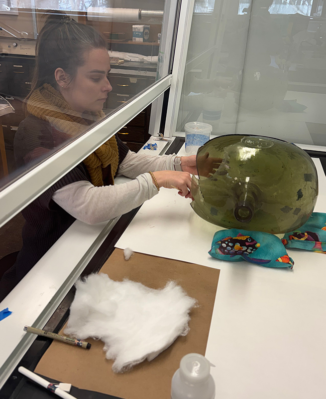 A graduate student in a labotory applies solvent to a green glass jar inside a fume hood.  