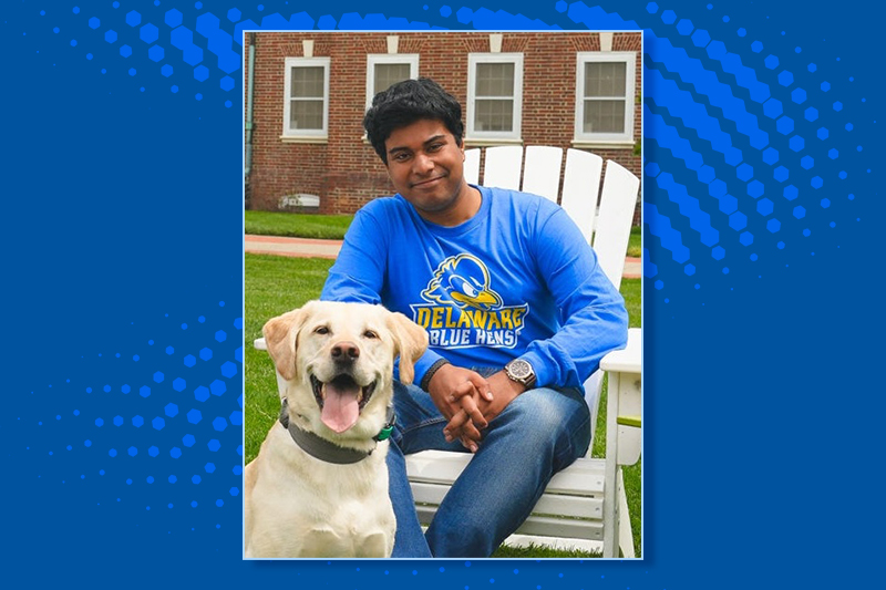 A college student and a white labrador retriever sit together on the The Green at the University of Delaware.