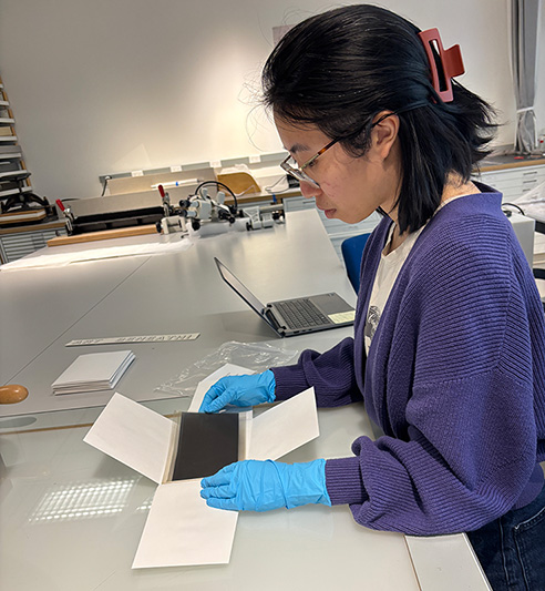 A college student wearing blue gloves in a laboratory inspect photo negatives on a work table.