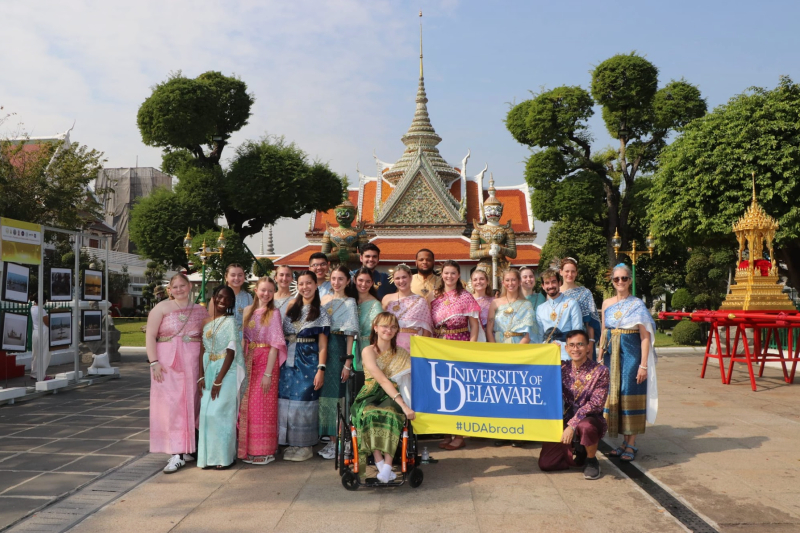 A group of smiling students and chaperones gather for a group photo in front of a temple in Thailand.