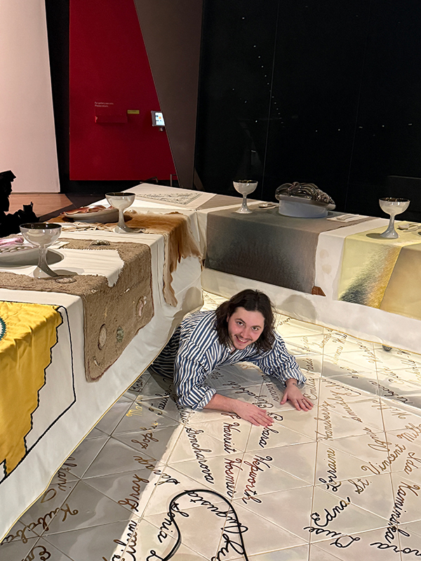 A graduate student lying on the floor while maintaining a large modern art installation by Judy Chicago.