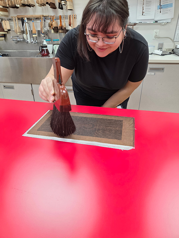 A graduate student in art laboratory uses a brush to mount a Japanese painting.