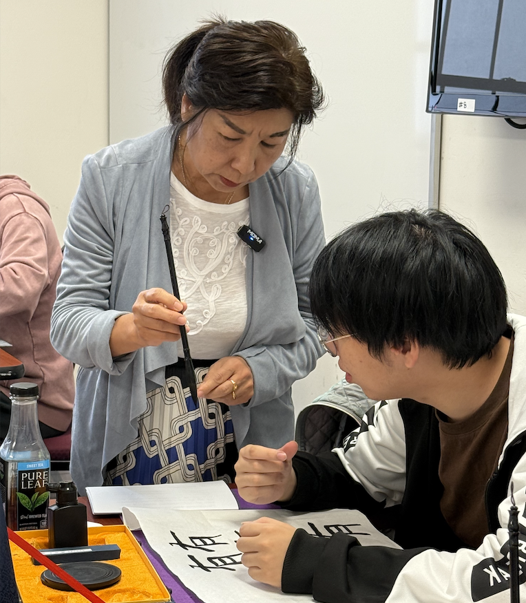 Lanzhu holds a calligrahy brush to show a student how to use it on calligraphy paper.