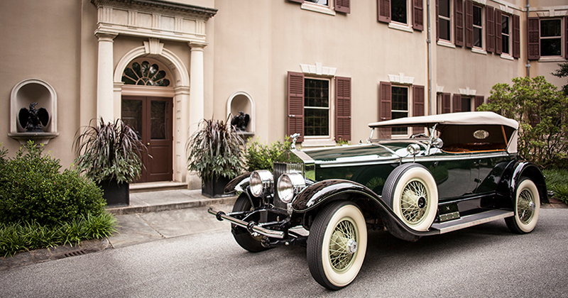 A green 1927 Rolls Royce car parked in front of a historic home.