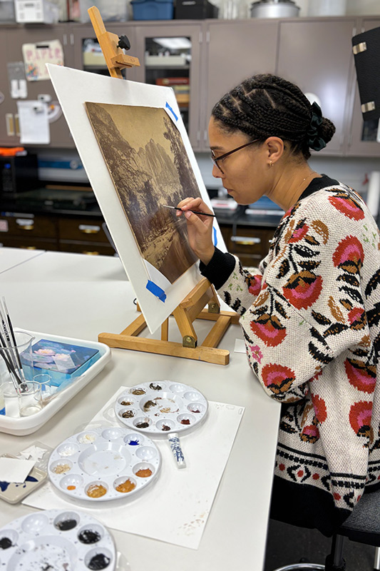 Michaela inpainting a loss on one of her second-year projects, a landscape of Yosemite Falls.