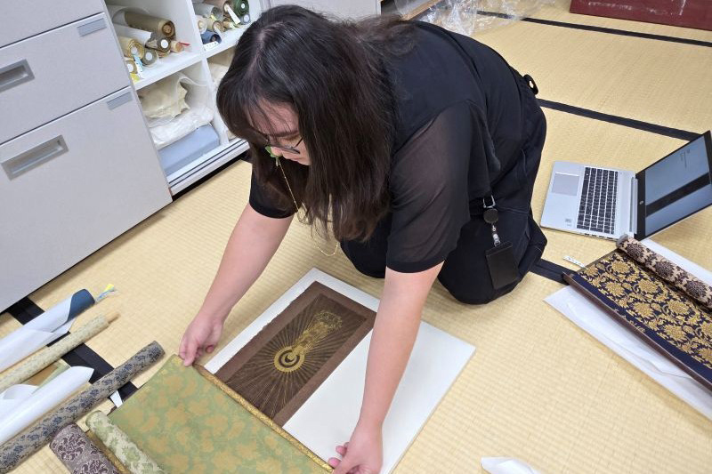 Sam considers new decorative fabric borders for the painting, a process called “toriawase” (取り合わせ). 