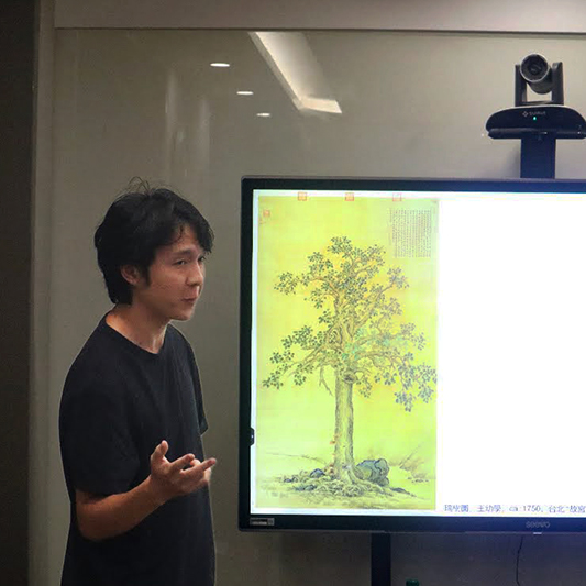 A college student in a conference room discusses a slide of the Auspicious Tree.