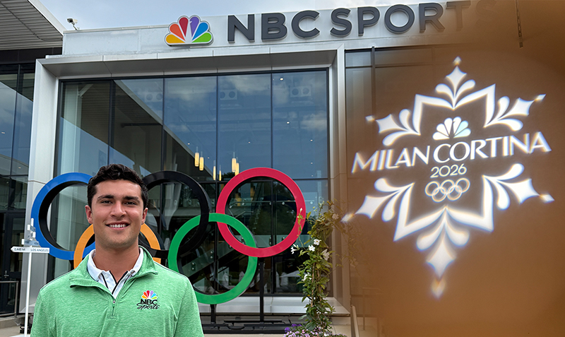 A smiling college student stands in front of the NBC Sports Building with the Olympic rings in front, with the Milan Olympics logo over a brown background partially covering the image