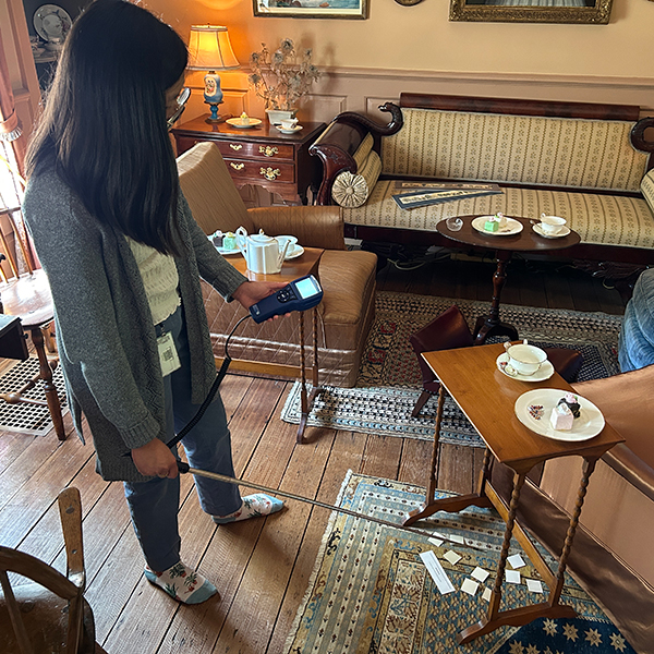 A college intern holds a meter will conducting a test inside a museum gallery.
