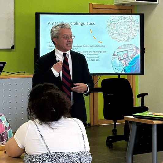 A professor in the front of a classroom delivers a lecture to students.